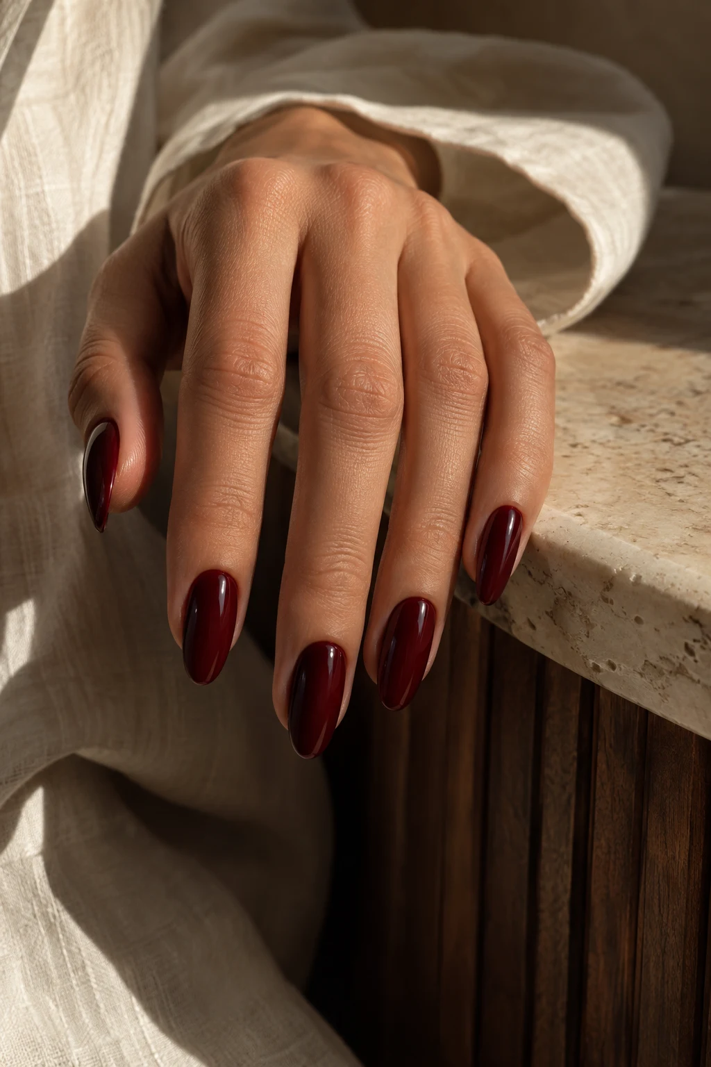 Editorial deep burgundy almond manicure against linen and stone